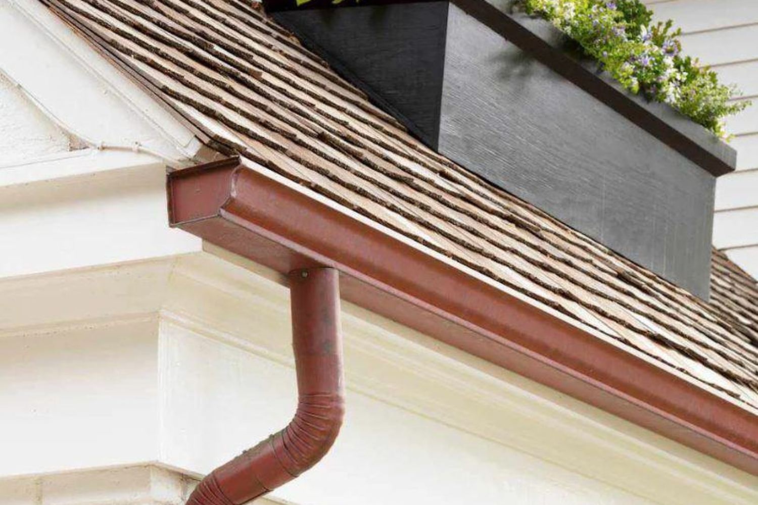 Copper downspout running down a white brick wall